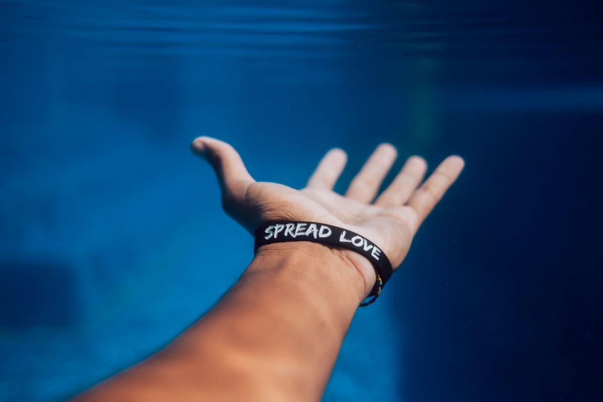 Leadership demonstrated with image of mn wearing "Spread Love" bracelet with hand outstretched, underwater.